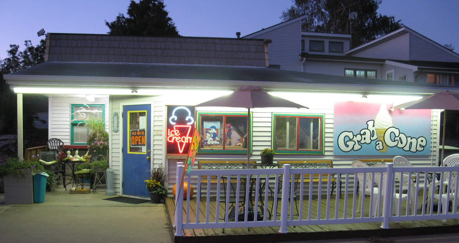Small business with a neon ice cream sign, fenced patio with tables, & sign reading Grab A Cone.