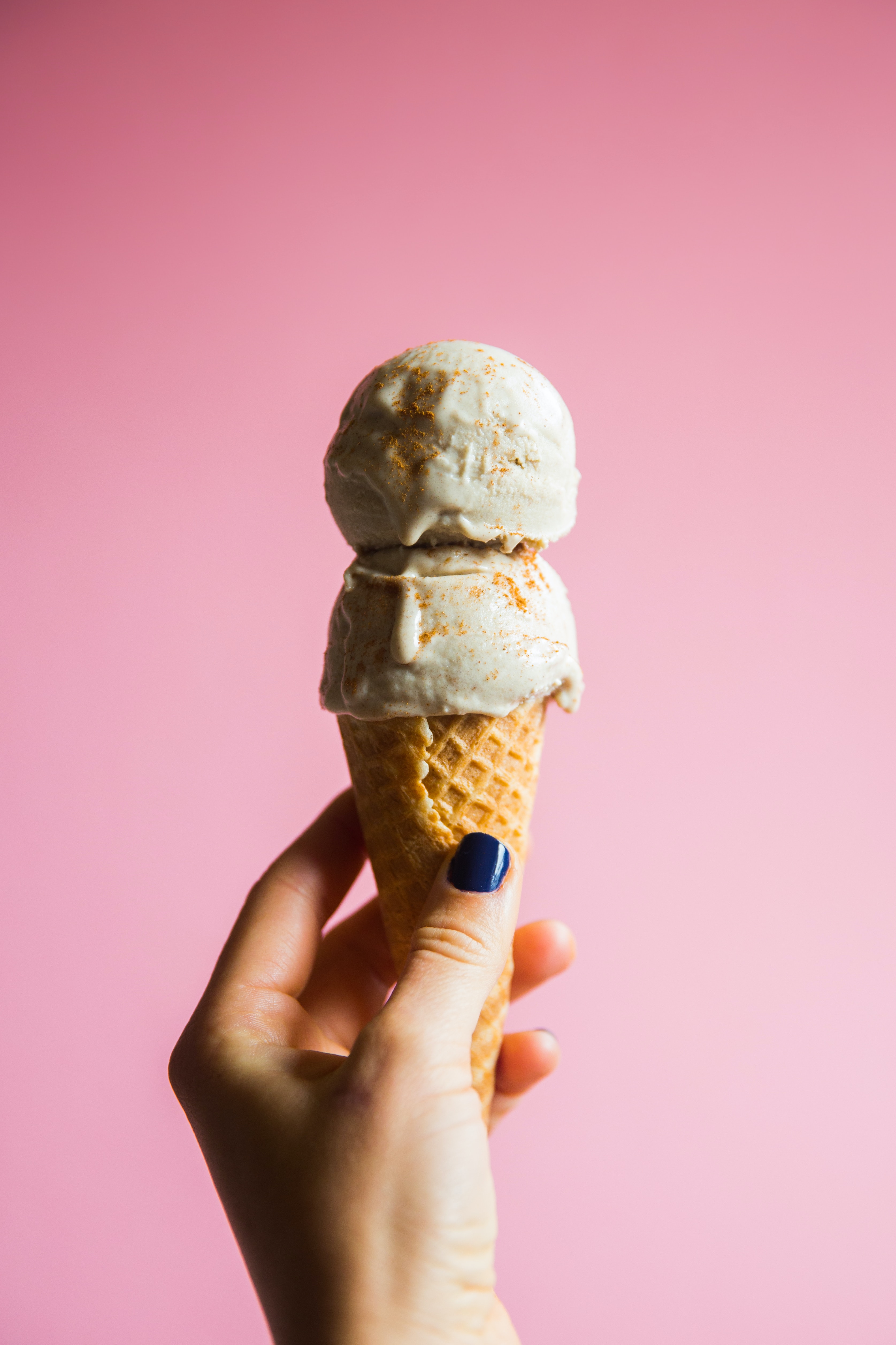 2 scoops of ice cream on a sugar cone with a pink background.